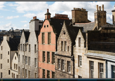 A row of houses with chimneys with a lone pink house in the middle. 